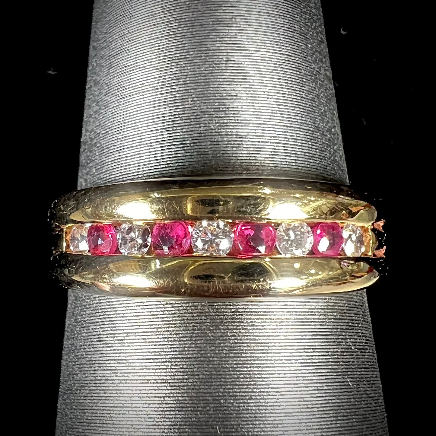 An 18kt yellow gold band channel set with round cut rubies and diamonds.