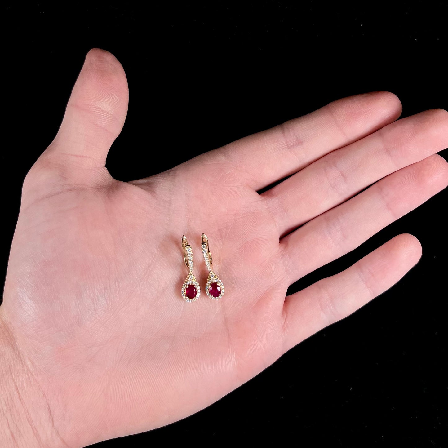 A pair of ruby and diamod halo dangle earrings cast in 14k yellow gold.