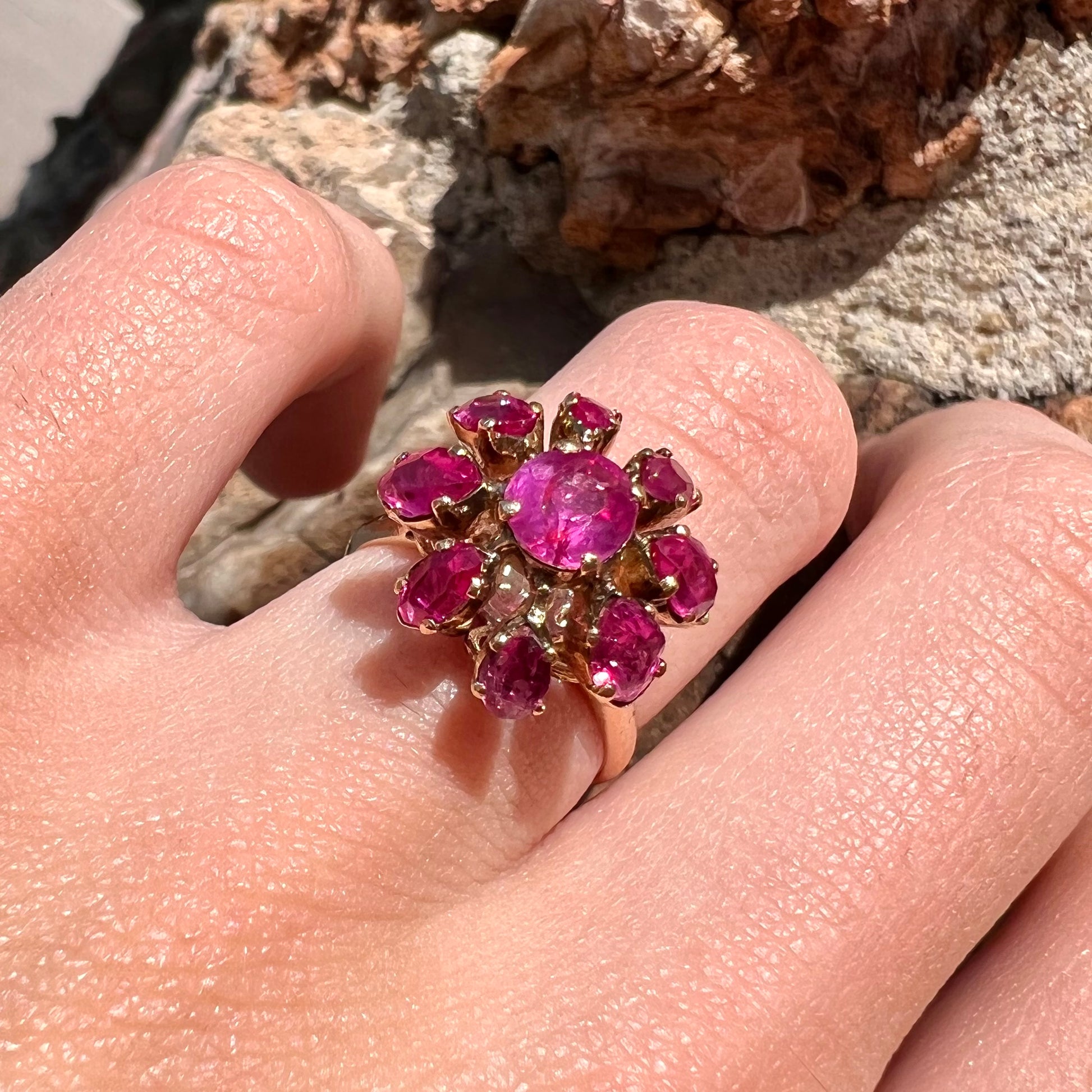 A yellow gold pink Burma ruby cluster ring with a faceted oval center stone surrounded by marquise cut stones.