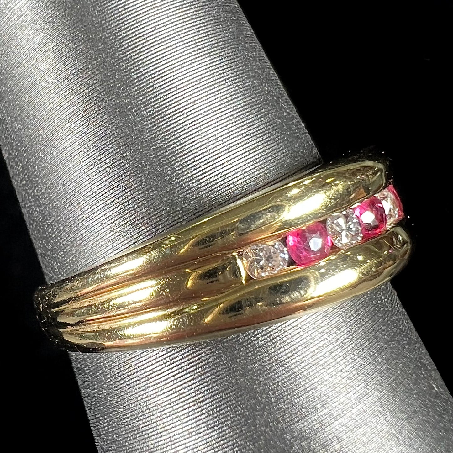 An 18kt yellow gold band channel set with round cut rubies and diamonds.