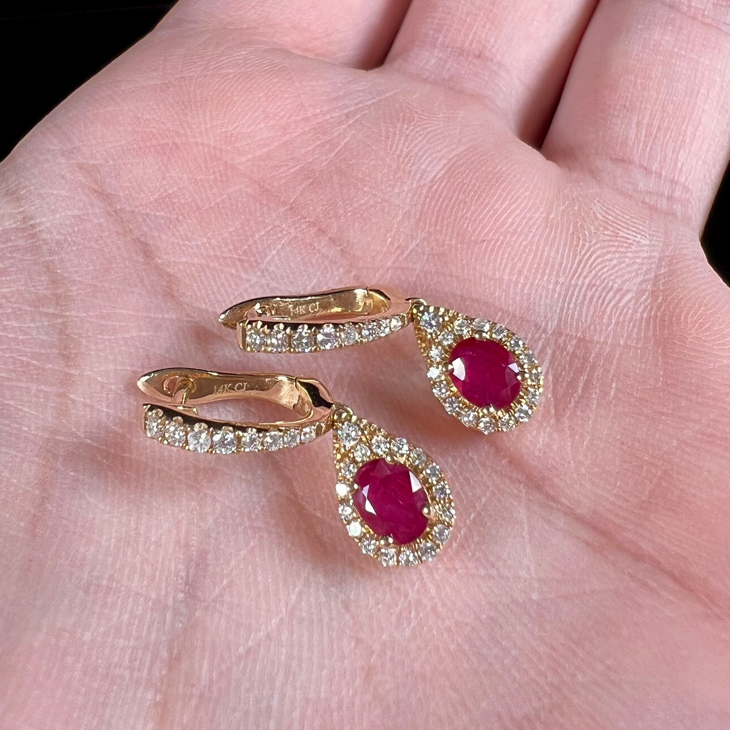 A pair of ruby and diamod halo dangle earrings cast in 14k yellow gold.