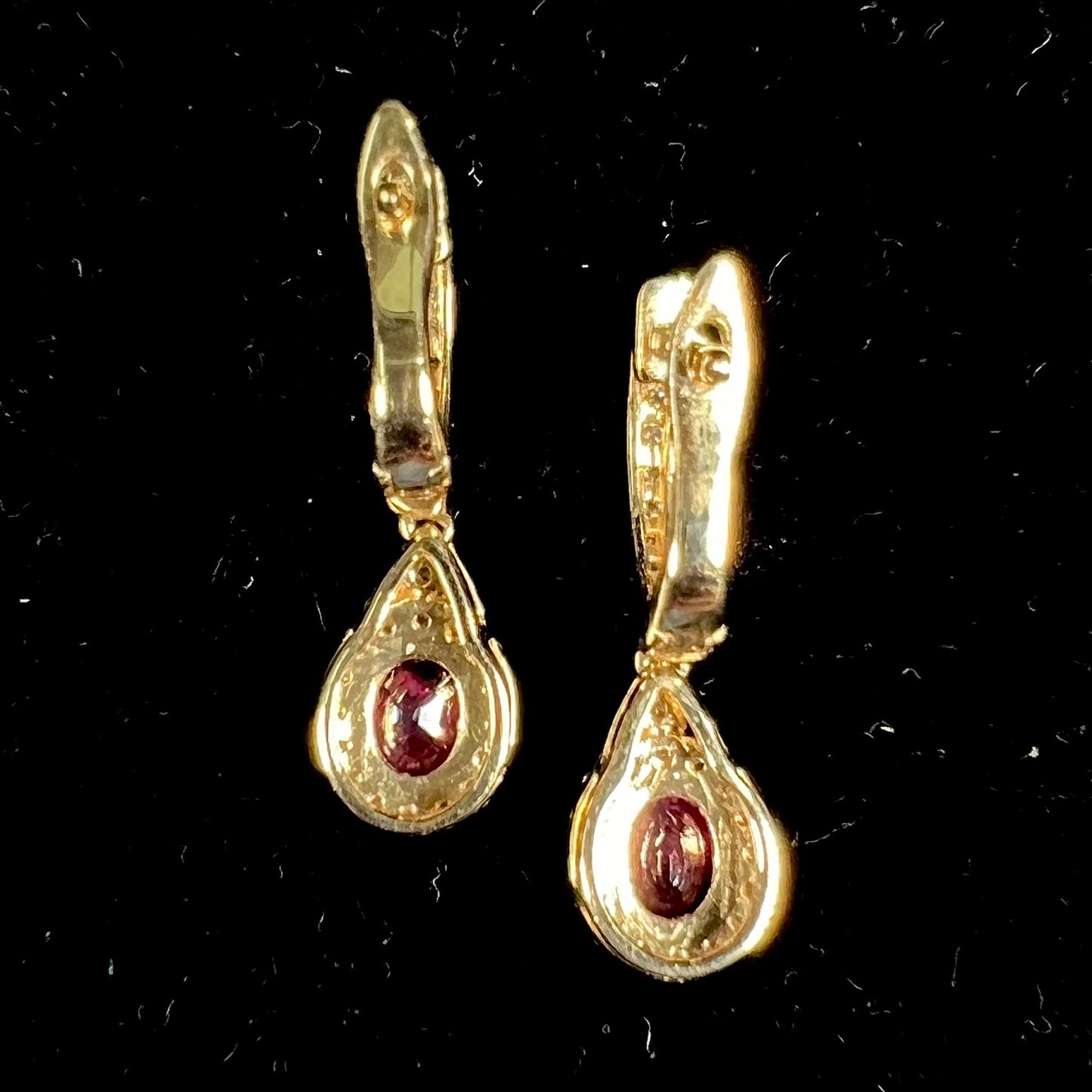 A pair of ruby and diamod halo dangle earrings cast in 14k yellow gold.