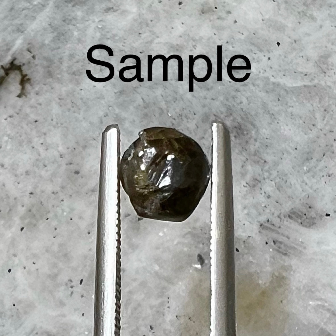 A single sample black diamond crystal held in steel tweezers.