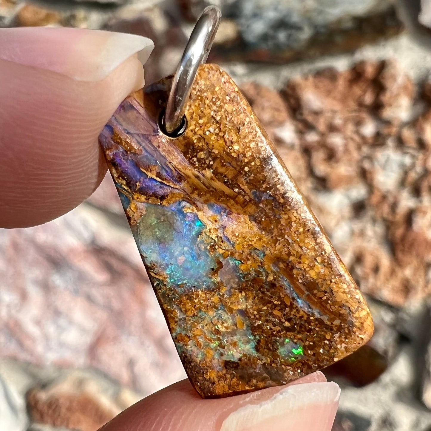 A drilled boulder opal stone with a sterling silver ring through the hole to be worn as a pendant.