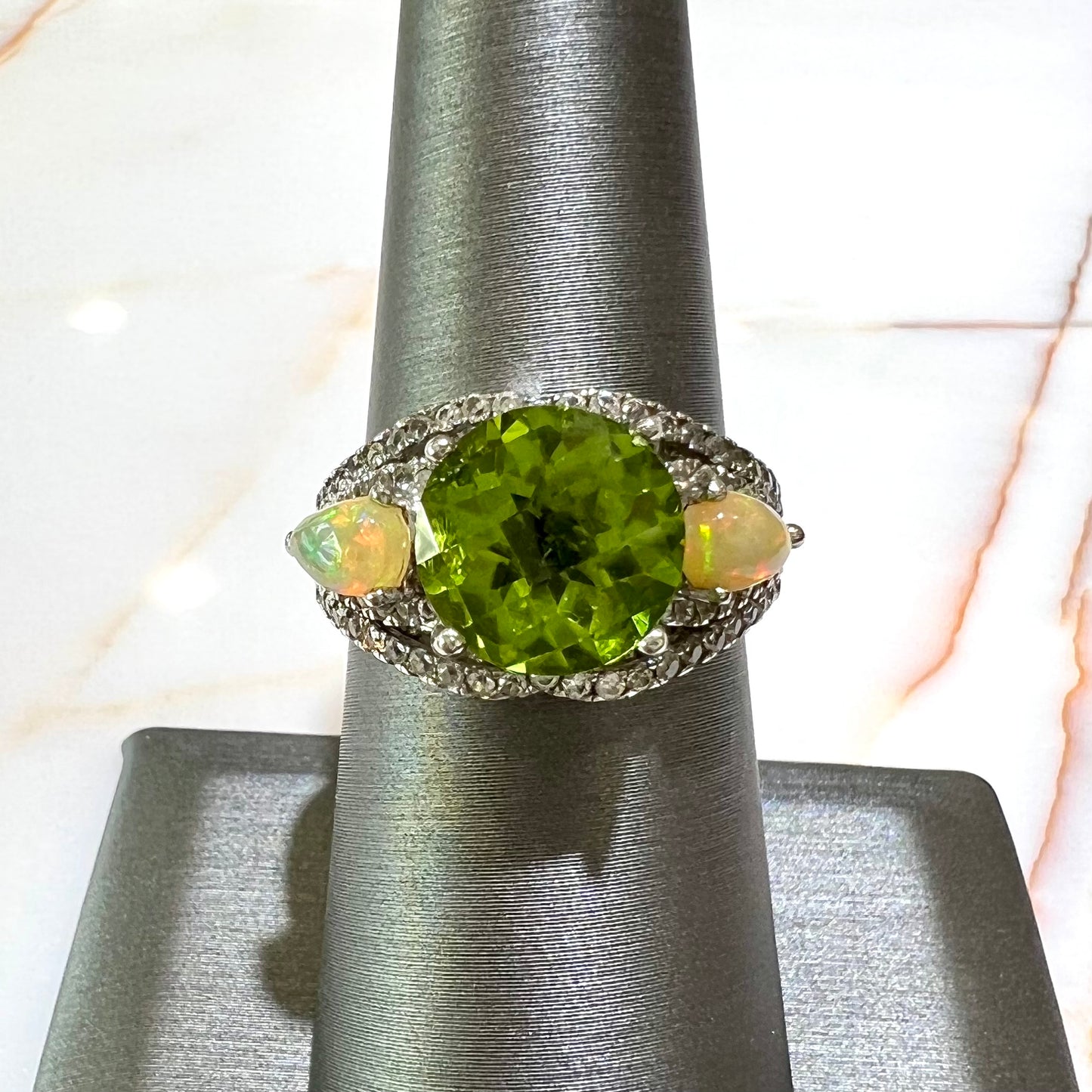 A sterling silver ring set with one large round peridot stone set between two pear shape cabochon Ethiopian opals. Cubic zirconia stones line the ring.