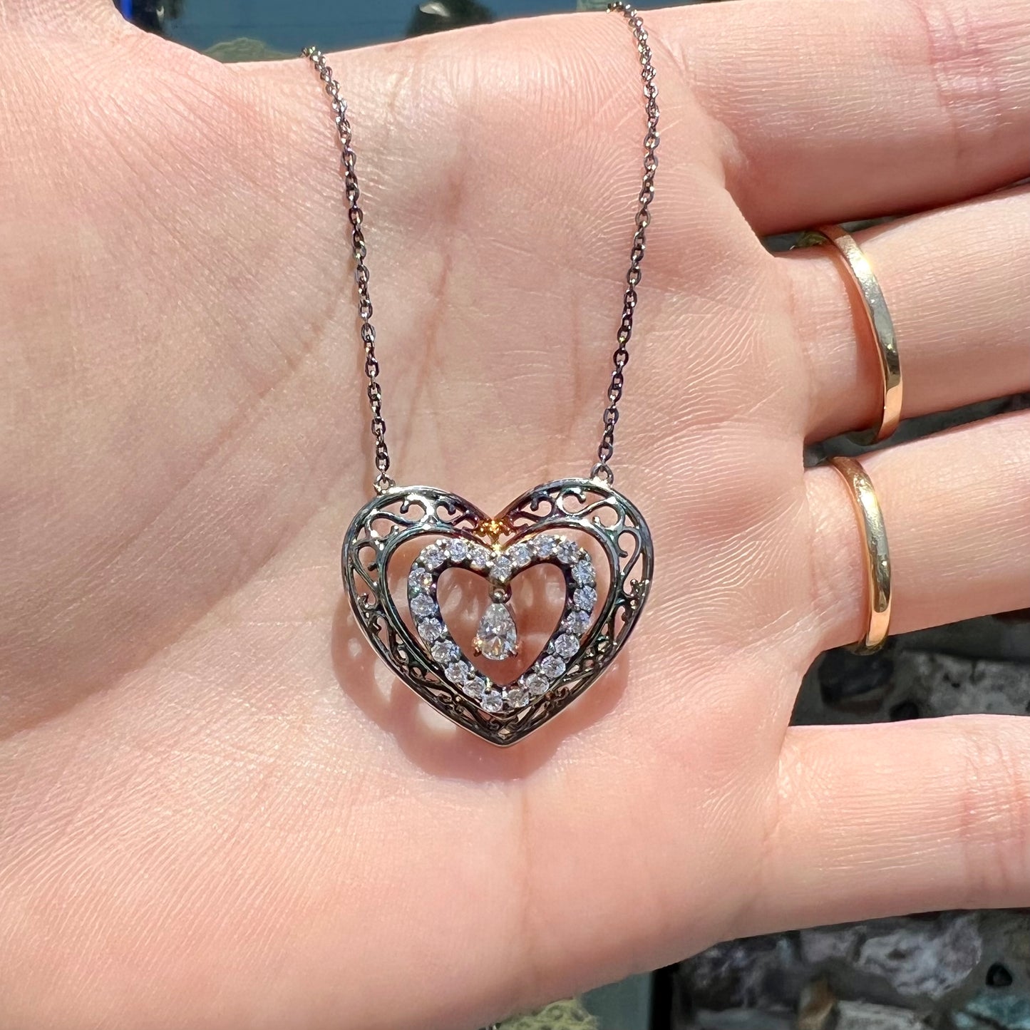 A sterling silver and cubic zirconia heart necklace. The silver has a rainbow patina.