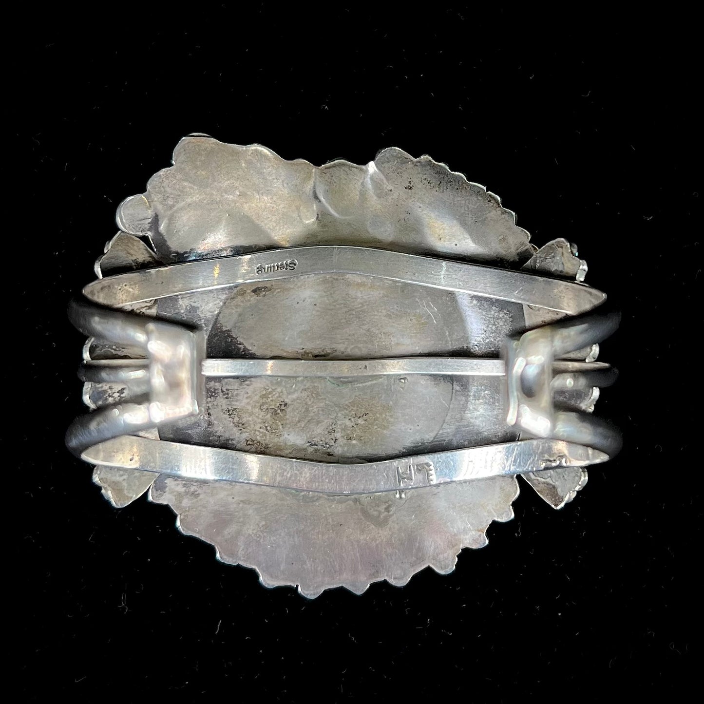 A sterling silver cuff bracelet featuring the motif of a stone inlaid hummingbird with petit point turquoise accents, handmade by Navajo artist Leo G. Harvey.