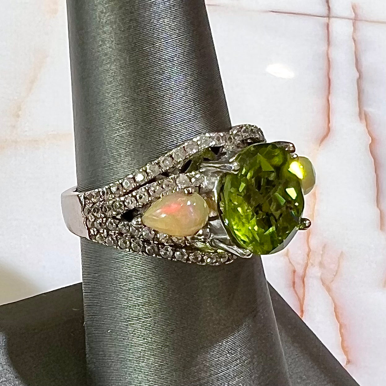 A sterling silver ring set with one large round peridot stone set between two pear shape cabochon Ethiopian opals. Cubic zirconia stones line the ring.