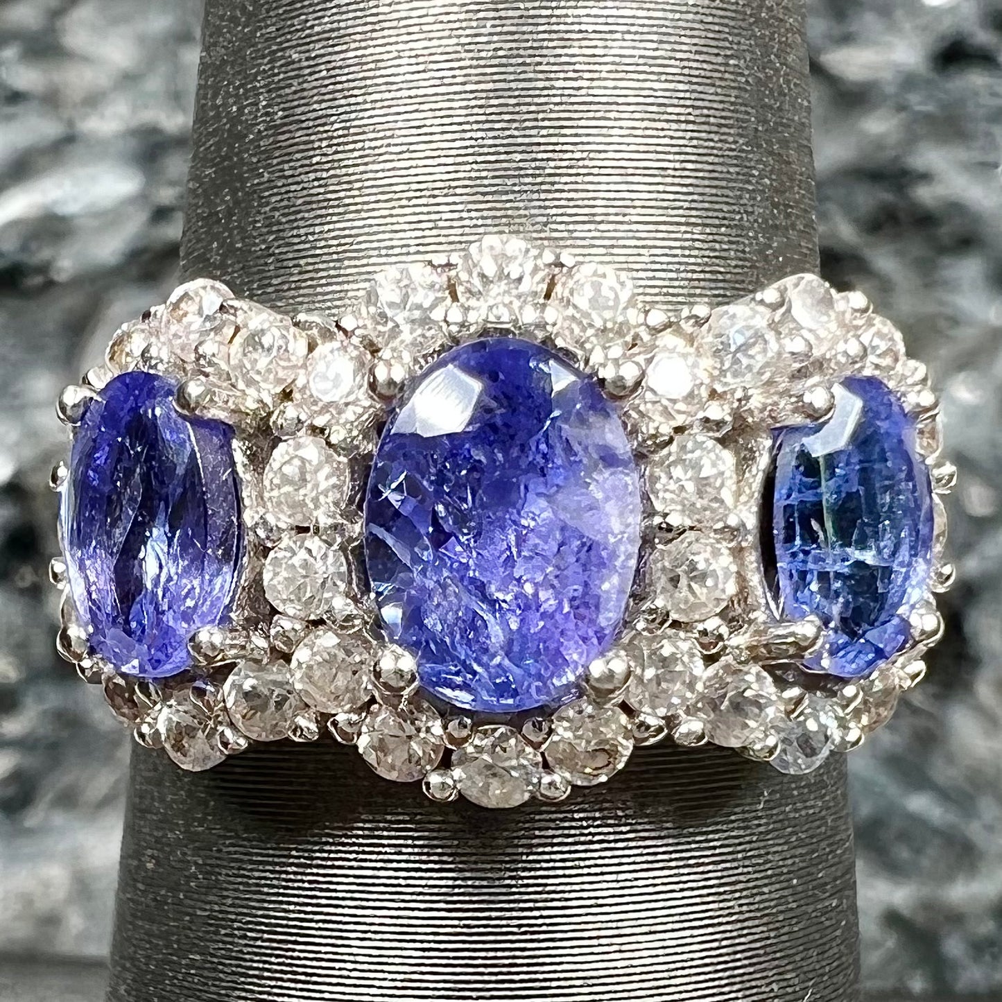 A sterling silver past, present, future three stone tanzanite ring. The main stones are set in a halo of cubic zirconia.