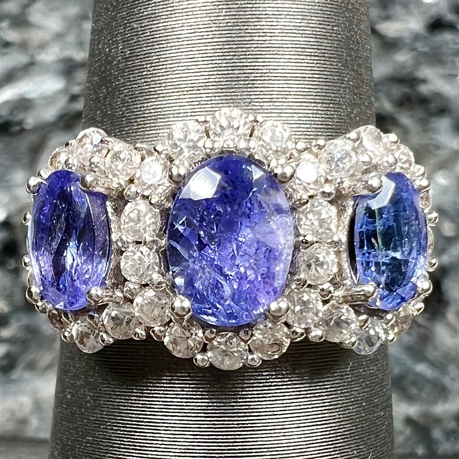 A sterling silver past, present, future three stone tanzanite ring.  The main stones are set in a halo of cubic zirconia.