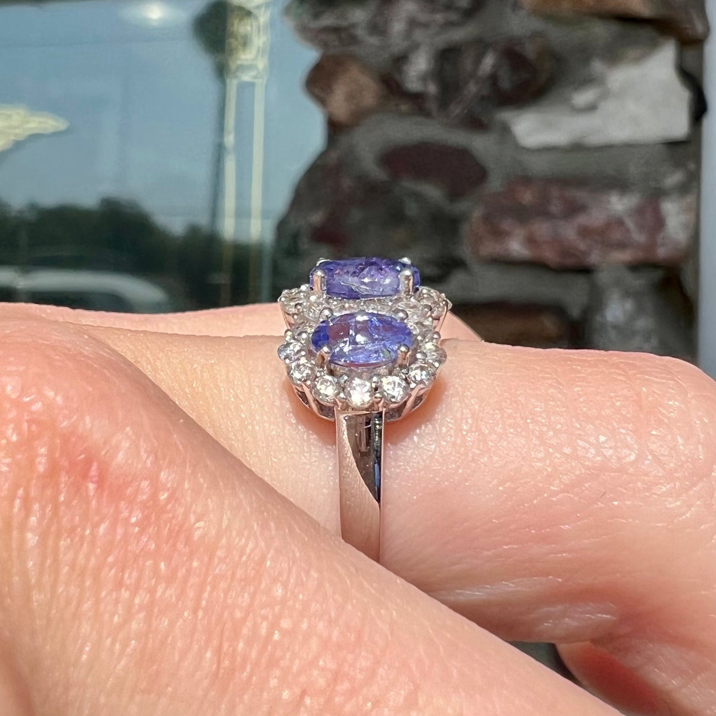 A sterling silver past, present, future three stone tanzanite ring. The main stones are set in a halo of cubic zirconia.