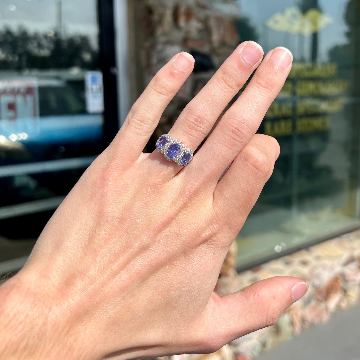 A sterling silver past, present, future three stone tanzanite ring. The main stones are set in a halo of cubic zirconia.