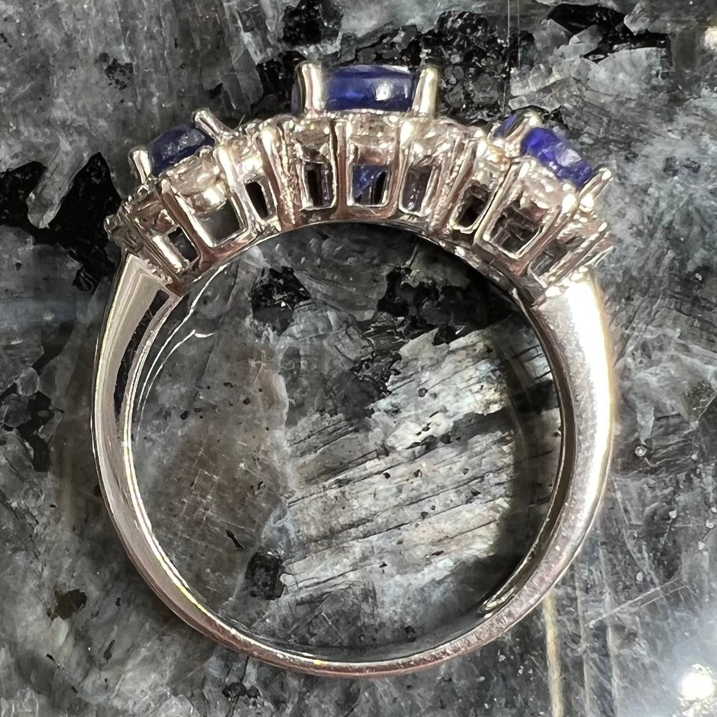 A sterling silver past, present, future three stone tanzanite ring. The main stones are set in a halo of cubic zirconia.