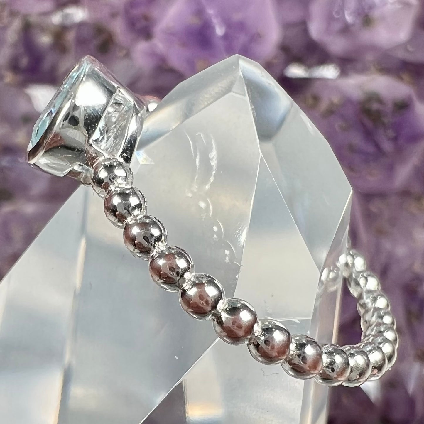A silver, bezel set, round cut sky blue topaz solitaire ring. The band is made of connected silver balls.