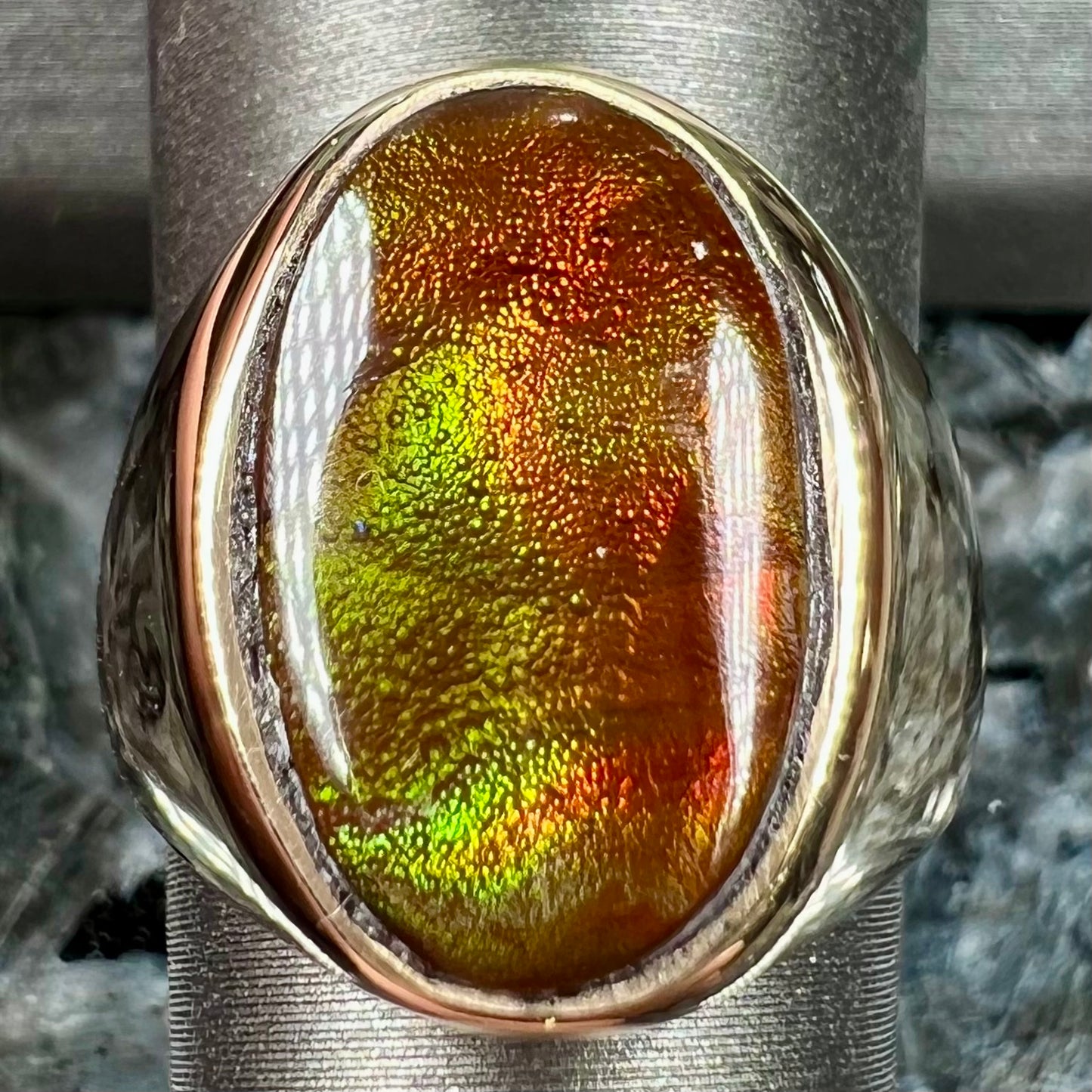 A yellow gold solitaire fire agate men's ring. The fire agate is oval shape, and red and green in color.