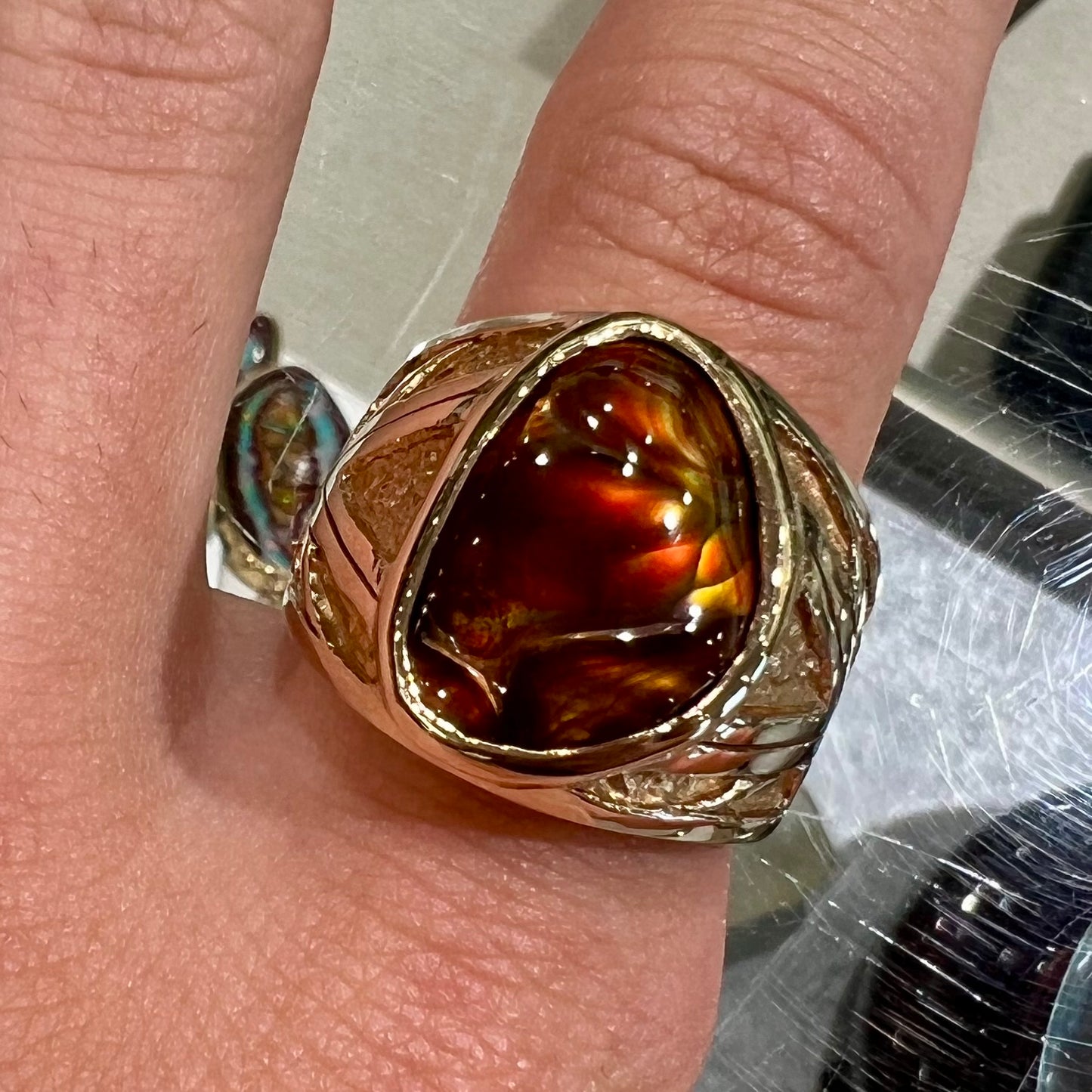 A solid, yellow gold men's fire agate ring. The predominant color is red with green undertones.
