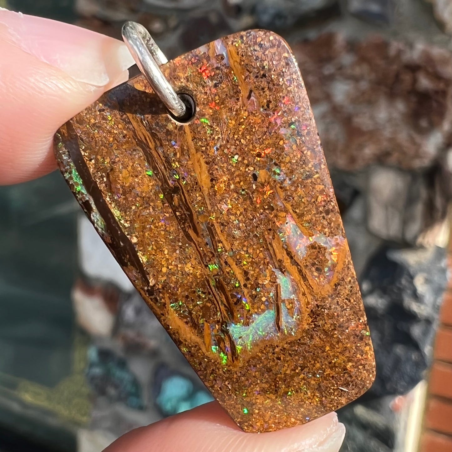 A drilled boulder opal stone with a sterling silver ring through the hole to be worn as a pendant.