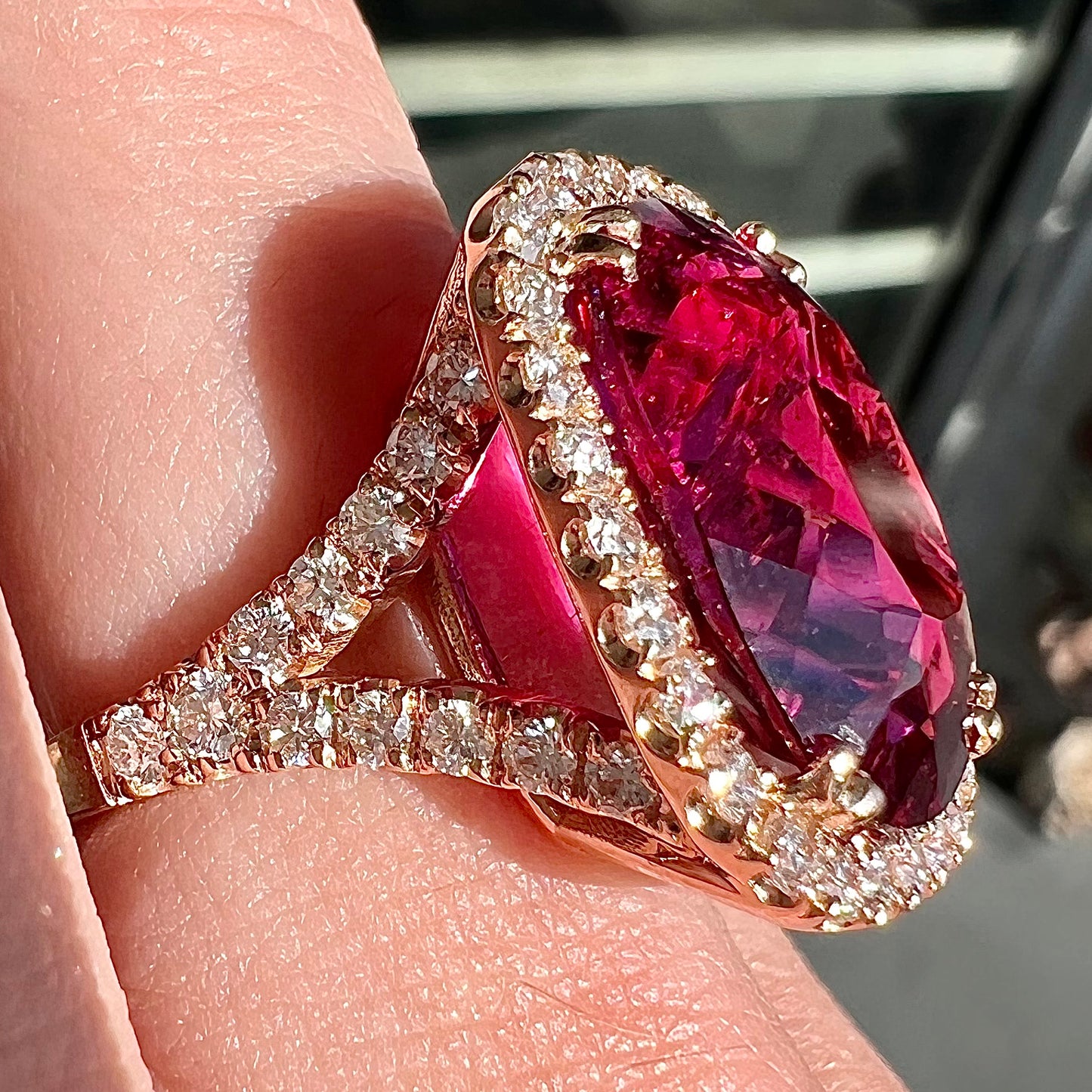 A rose gold, split shank engagement ring set with a cushion cut rubellite tourmaline in a diamond halo.