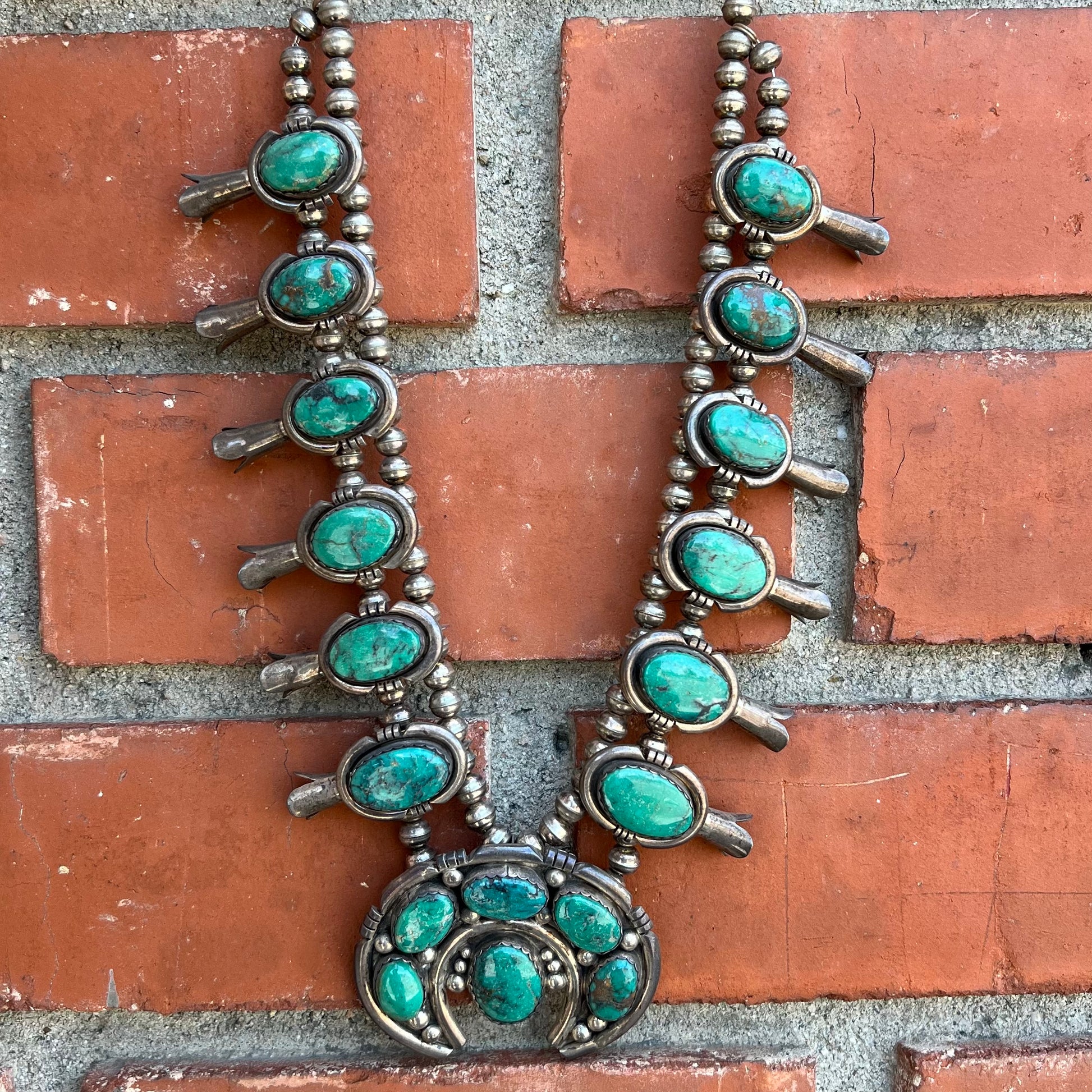A silver Kingman turquoise squash blossom necklace.  The necklace is made with handmade Navajo pearls.