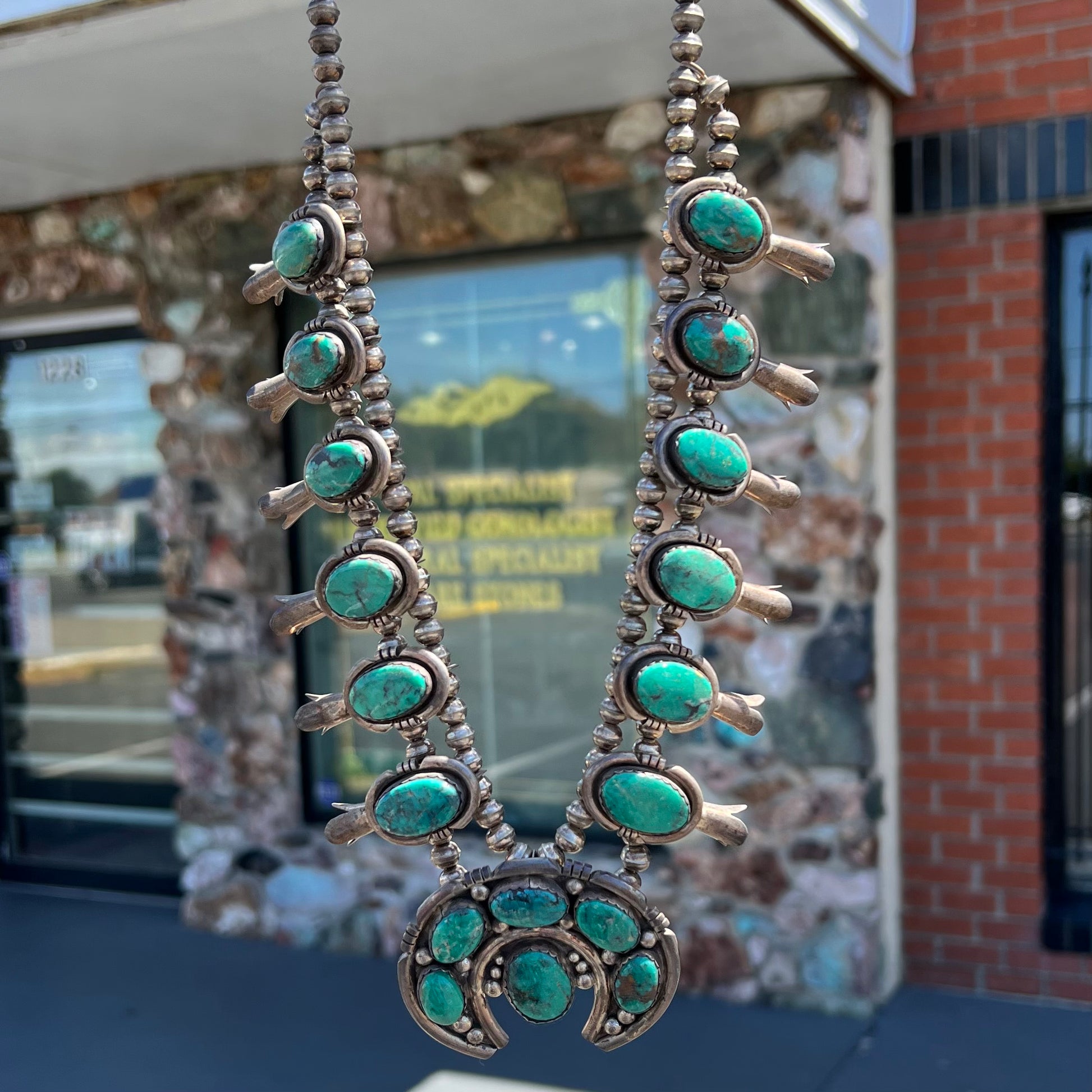 A silver Kingman turquoise squash blossom necklace.  The necklace is made with handmade Navajo pearls.