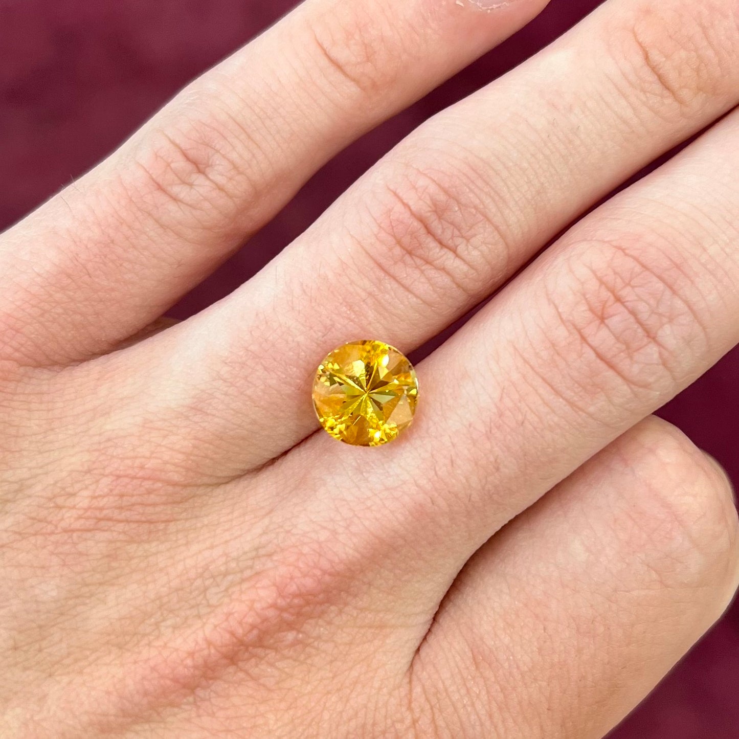 A loose, faceted round cut citrine stone with back facets that form a five pointed star.