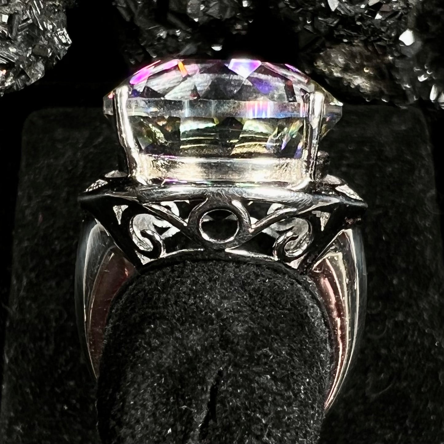 A large, round cut pink and green mystic topaz set in a sterling silver ring with white topaz accent stones.