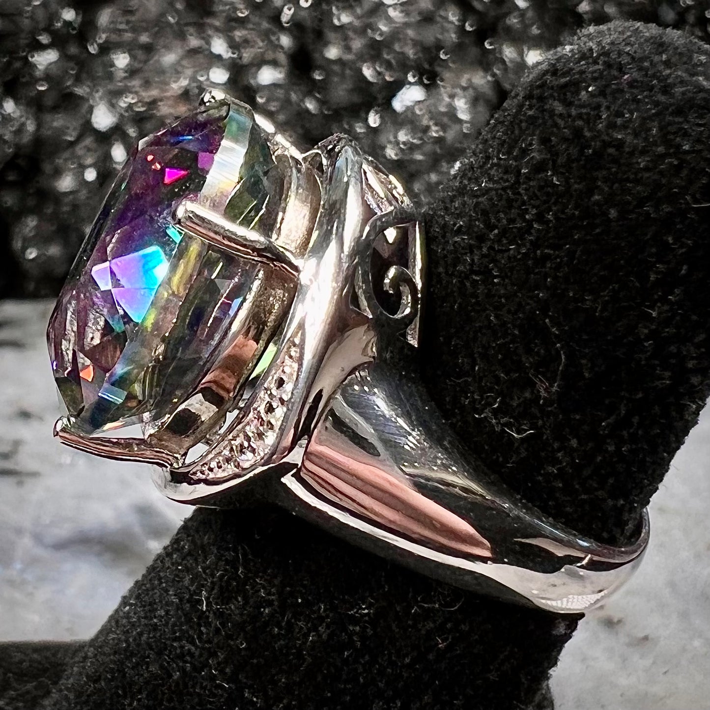A large, round cut pink and green mystic topaz set in a sterling silver ring with white topaz accent stones.