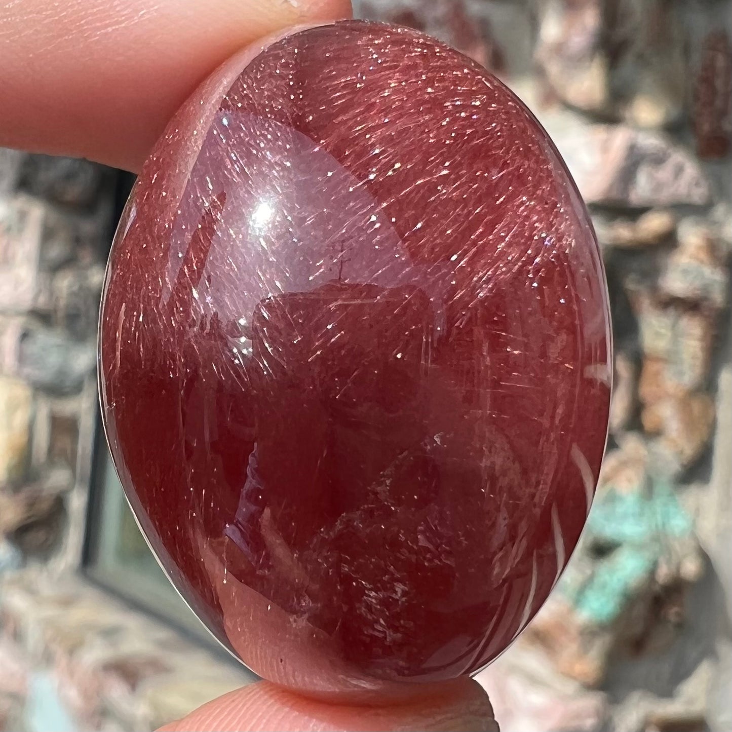 A large, oval cabochon cut strawberry quartz. The stone has a trapiche star-like pattern.