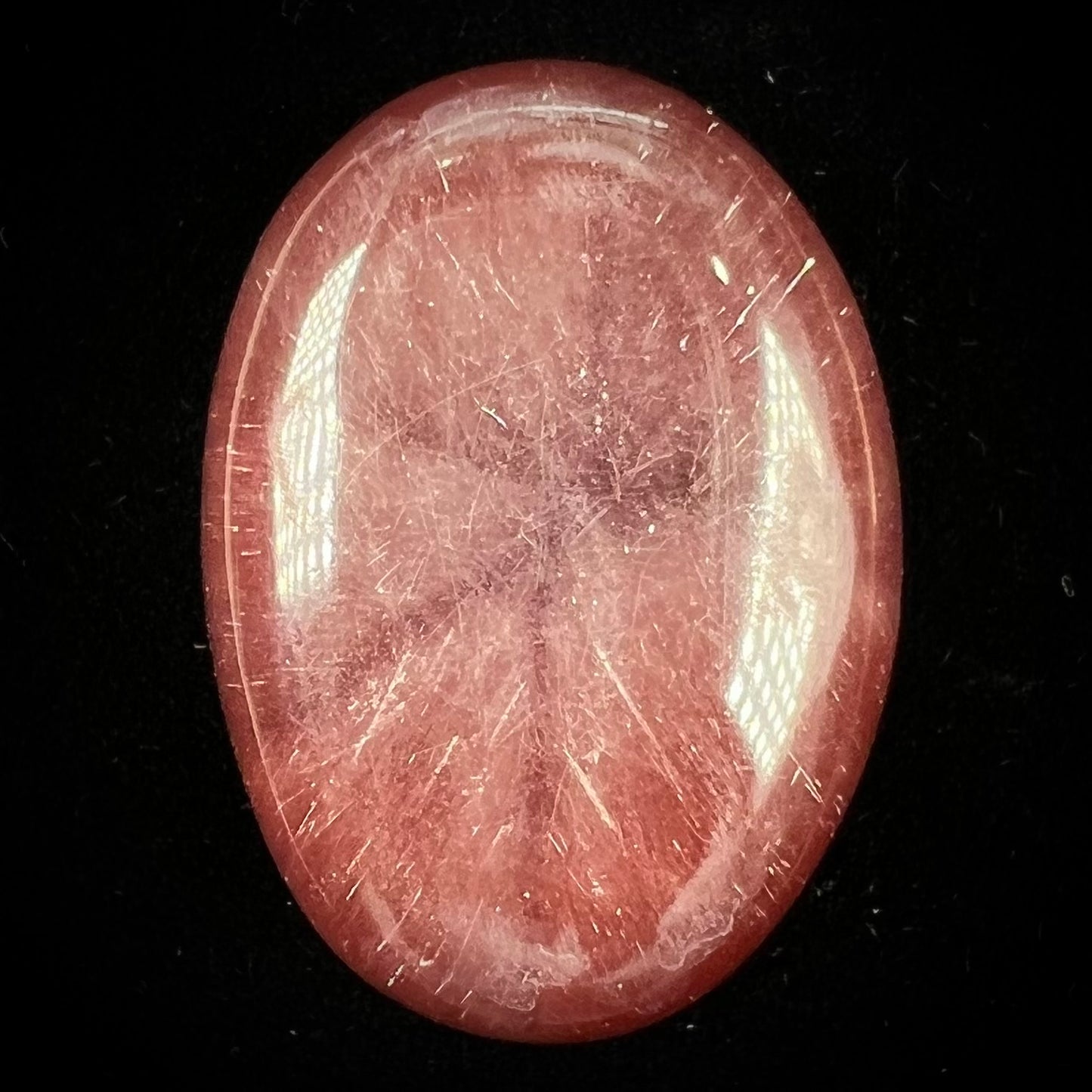 A large, oval cabochon cut strawberry quartz. The stone has a trapiche star-like pattern.