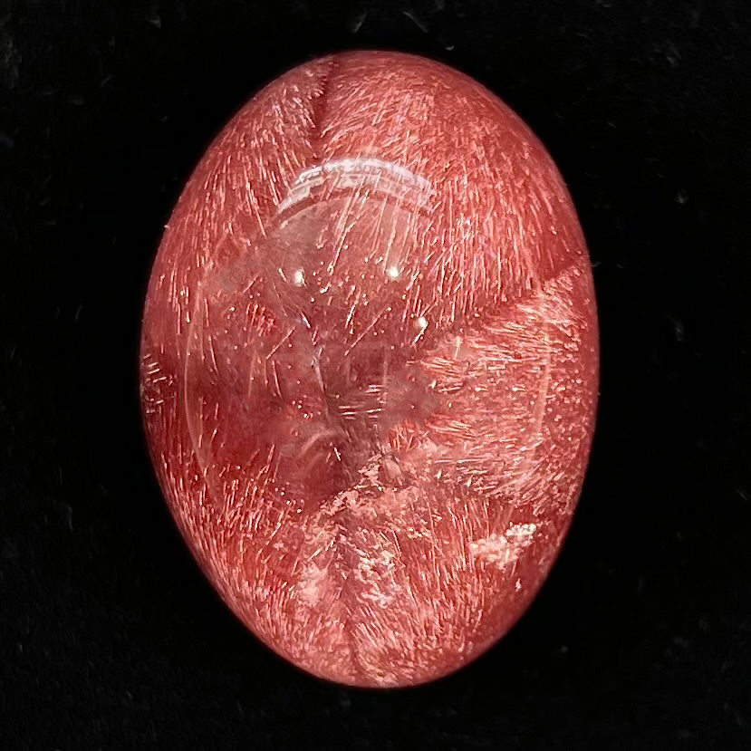A large, oval cabochon cut strawberry quartz. The stone has a trapiche star-like pattern.