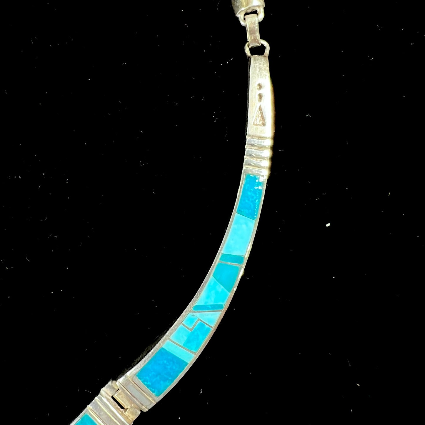 A silver omega style necklace inlaid with turquoise under the watch of David Rosales.