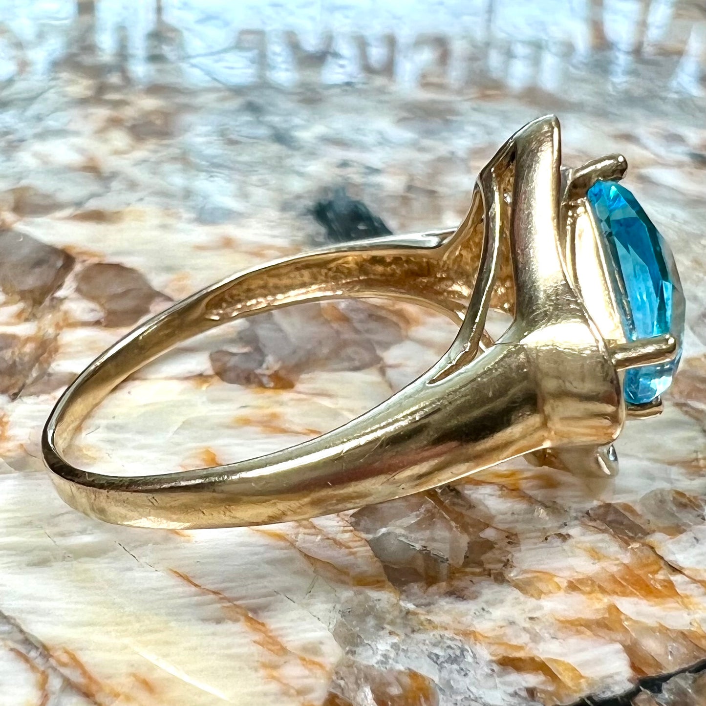 A checkerboard princess cut Swiss blue topaz ring. The stone is set in a yellow gold, diamond halo mounting.