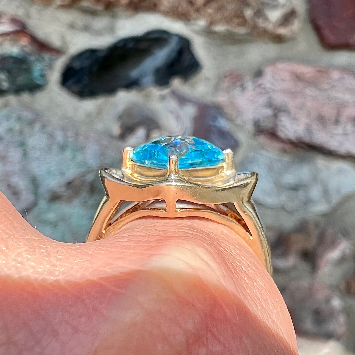 A checkerboard princess cut Swiss blue topaz ring. The stone is set in a yellow gold, diamond halo mounting.
