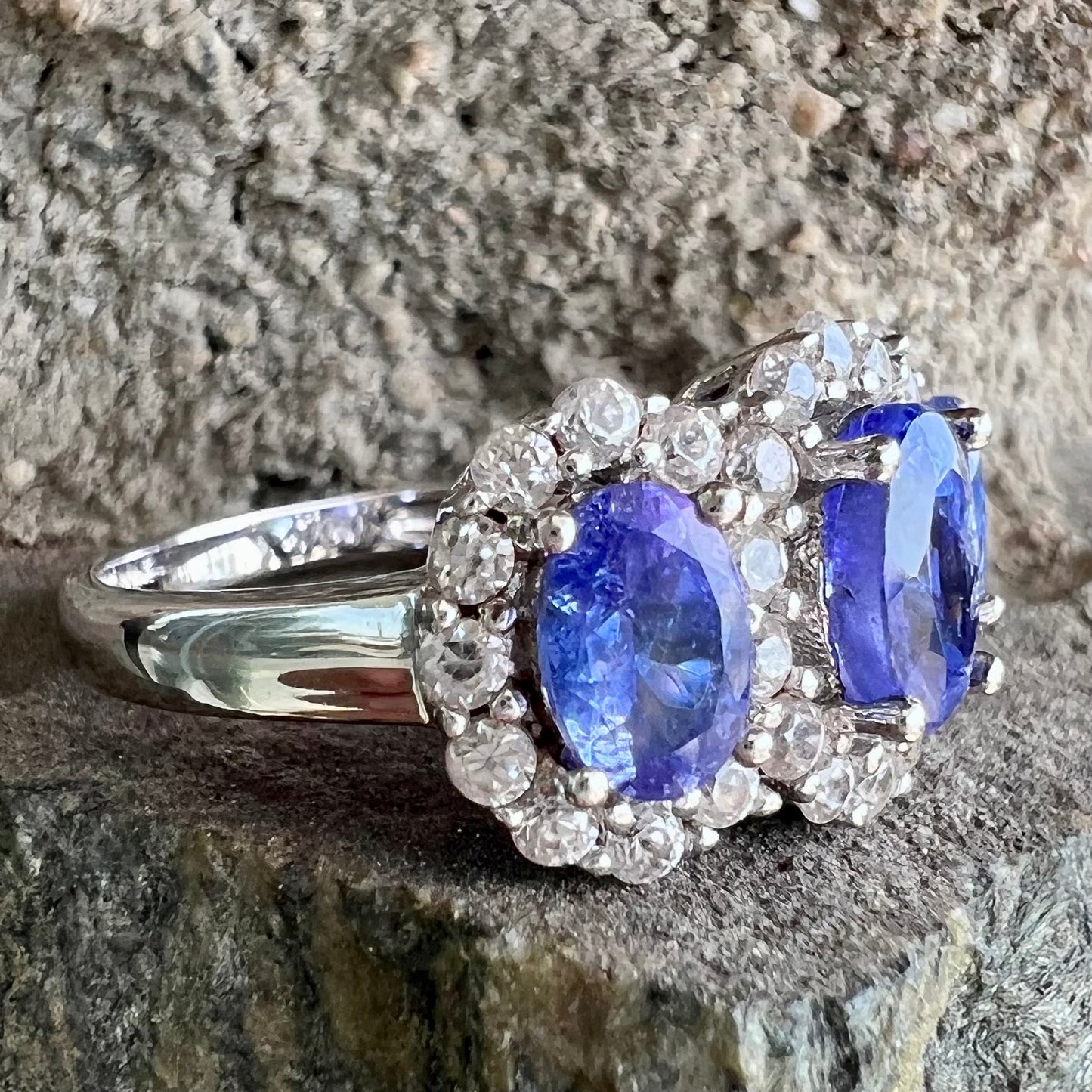 A sterling silver past, present, future three stone tanzanite ring. The main stones are set in a halo of cubic zirconia.