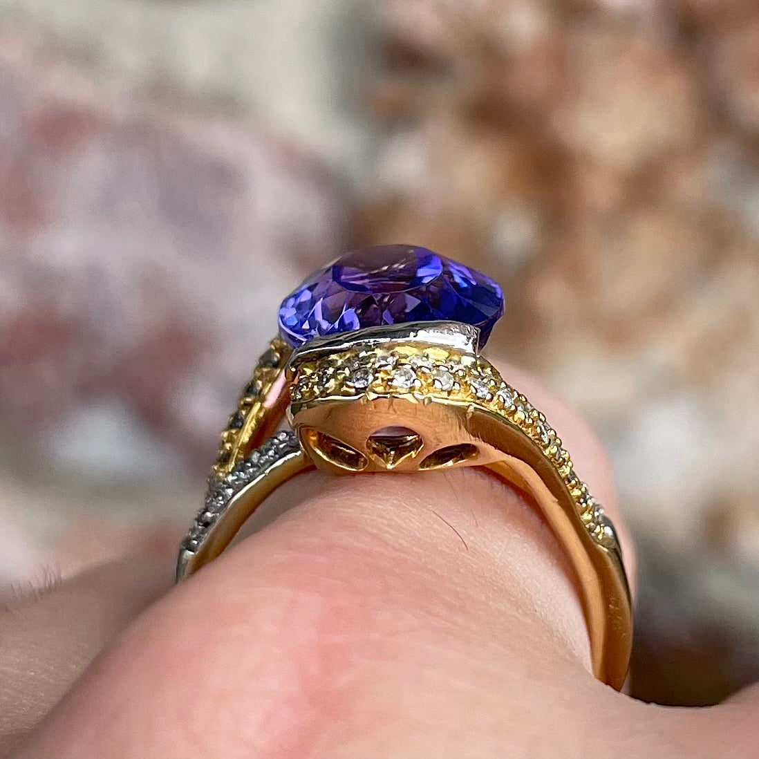 A large, oval cut blue tanzanite set in a two tone yellow and white gold diamond ring.