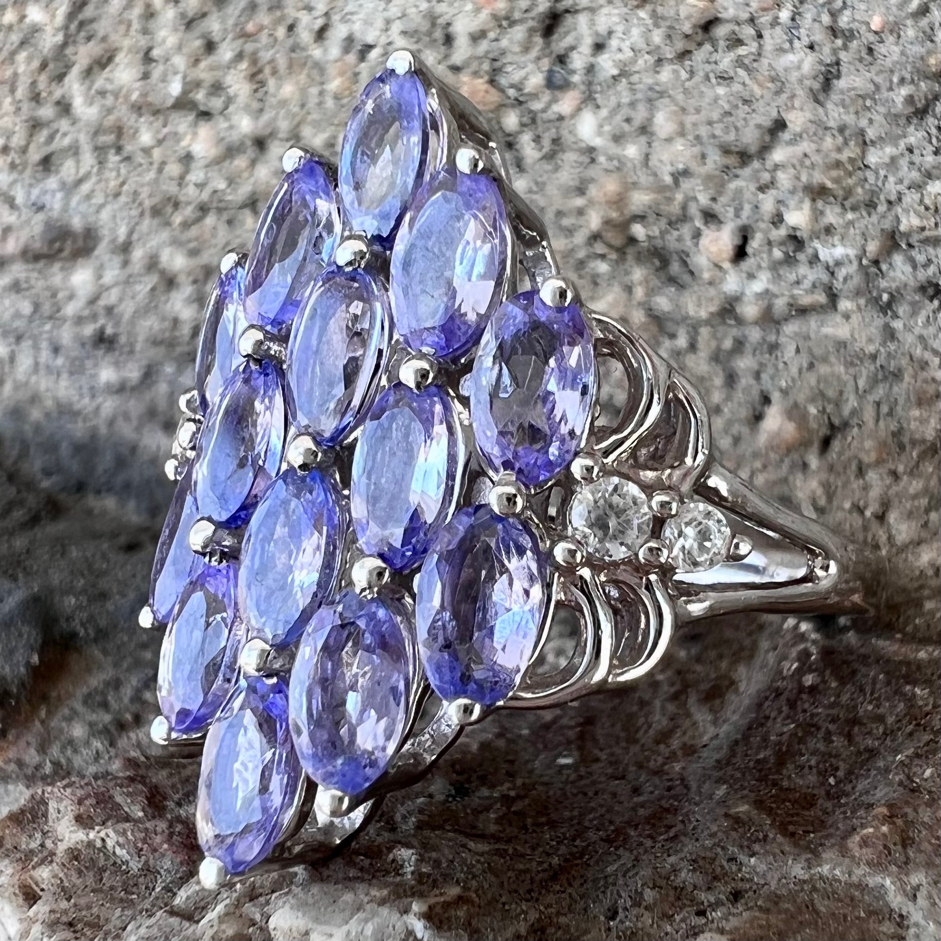 A sterling silver gemstone cluster ring set with oval cut tanzanite stones and round cubic zirconia accents.