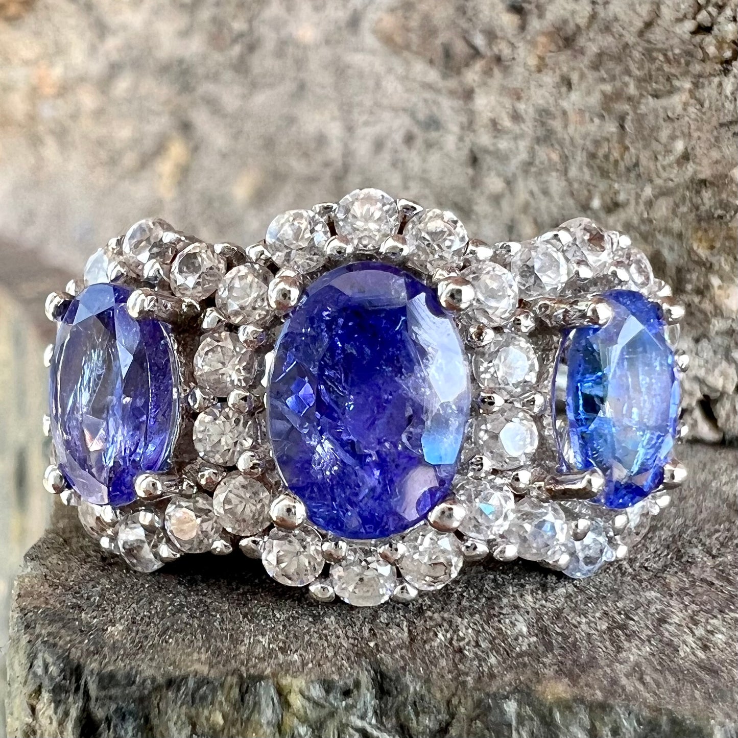 A sterling silver past, present, future three stone tanzanite ring. The main stones are set in a halo of cubic zirconia.