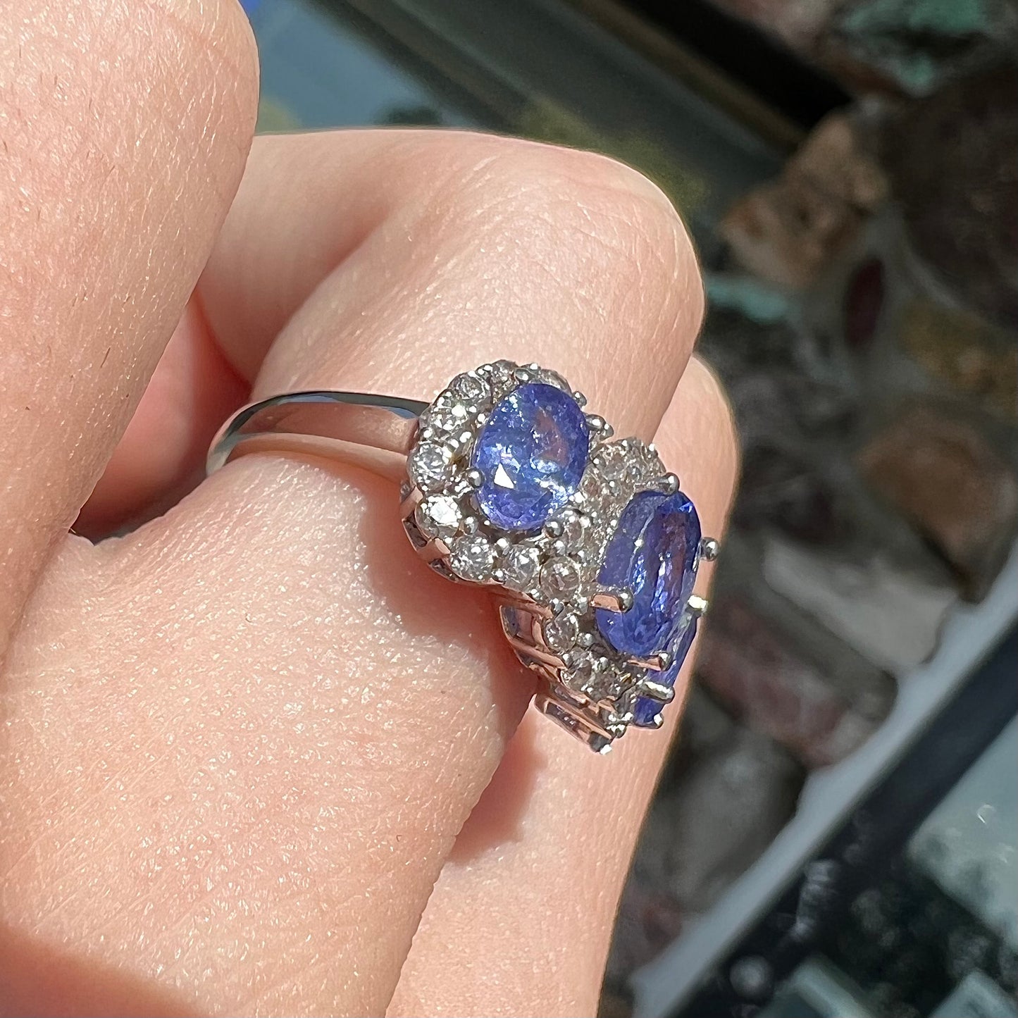A sterling silver past, present, future three stone tanzanite ring. The main stones are set in a halo of cubic zirconia.