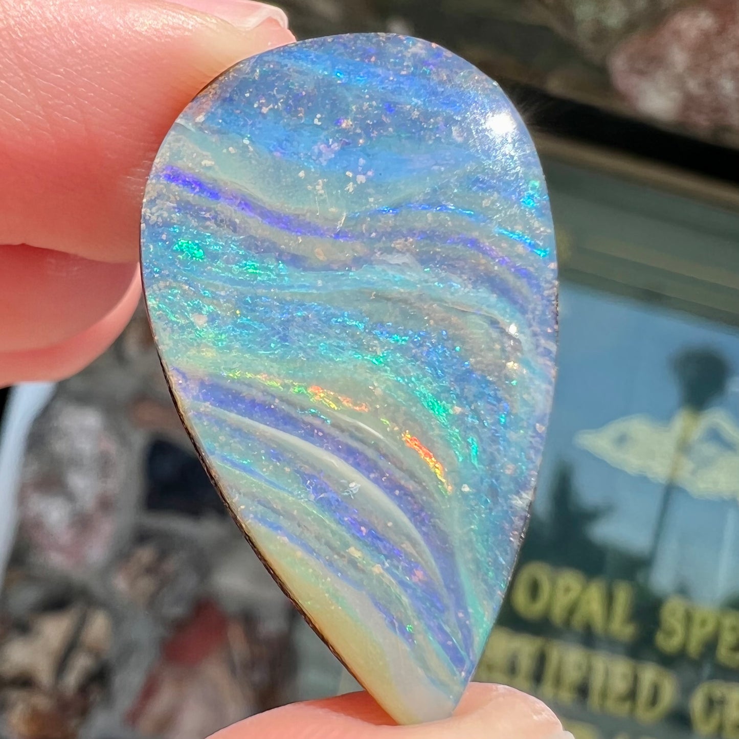 A loose, pear shaped boulder opal stone from Quilpie, Australia. The stone is predominantly blue, green, and purple with red and orange undertones.