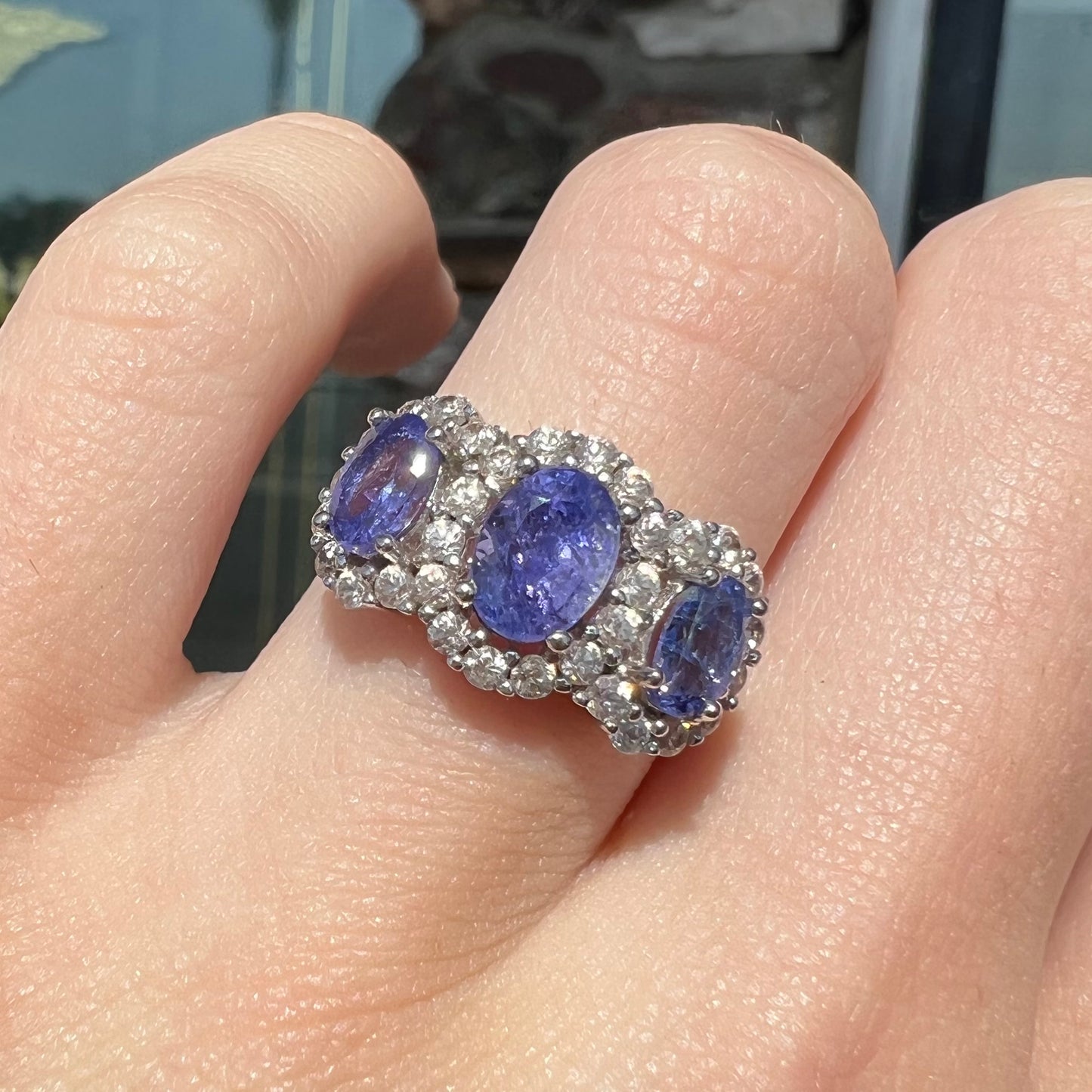 A sterling silver past, present, future three stone tanzanite ring. The main stones are set in a halo of cubic zirconia.