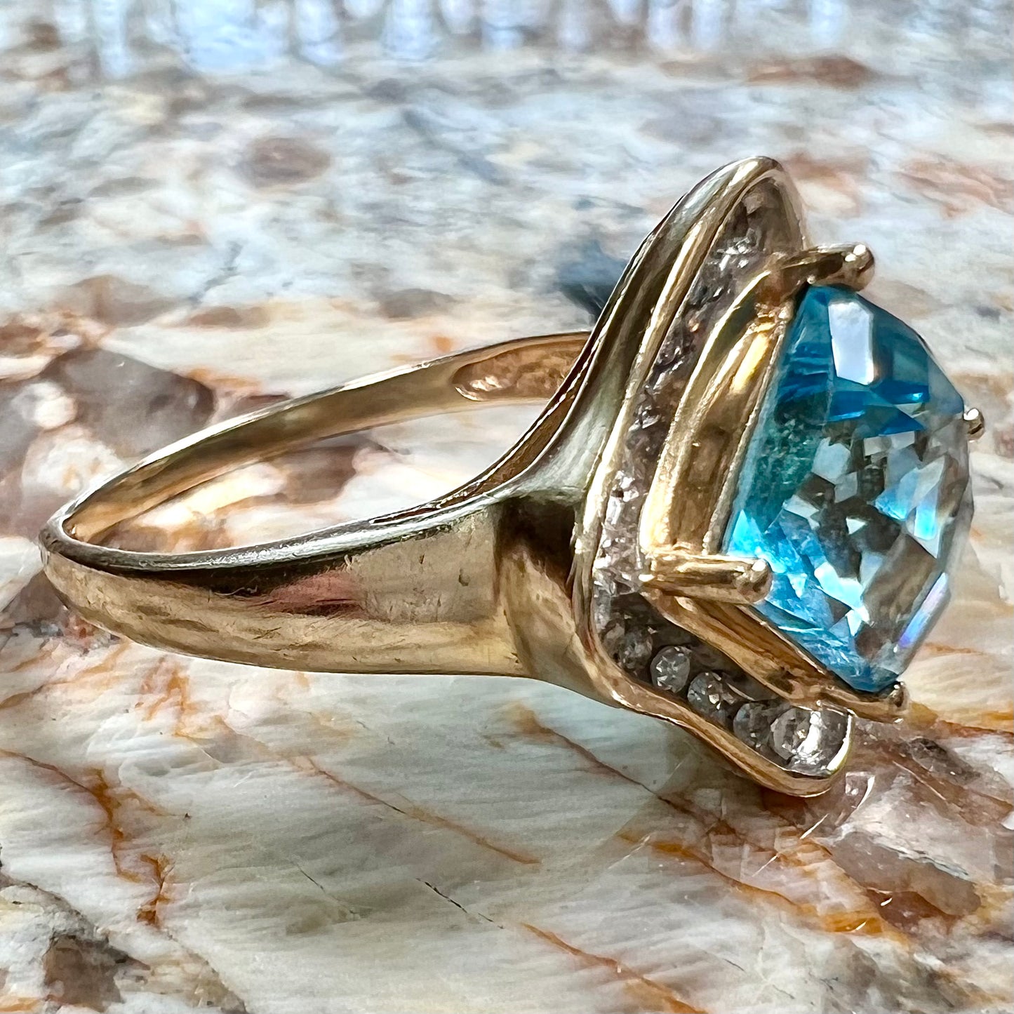A checkerboard princess cut Swiss blue topaz ring. The stone is set in a yellow gold, diamond halo mounting.