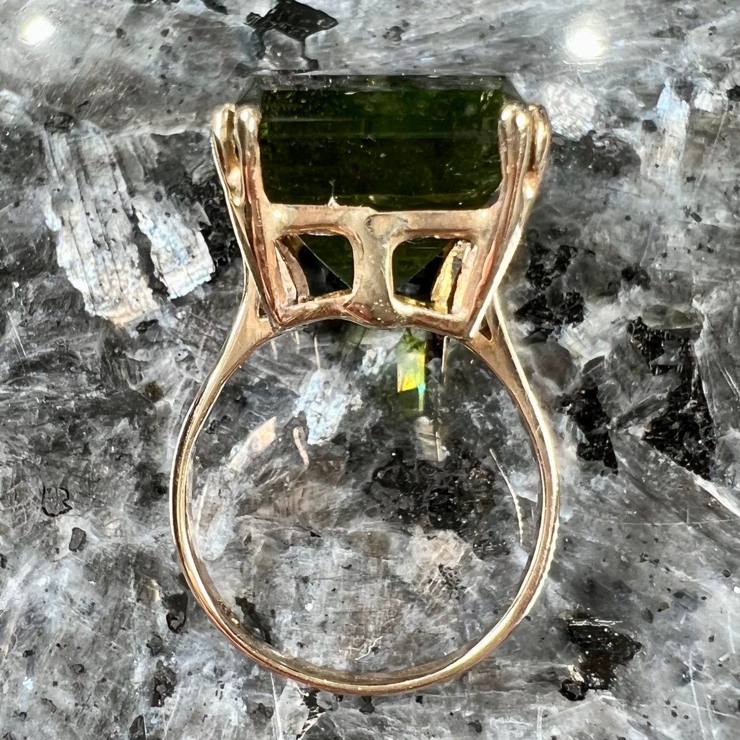 A faceted step-cut dark green tourmaline basket set solitaire ring cast in yellow gold.