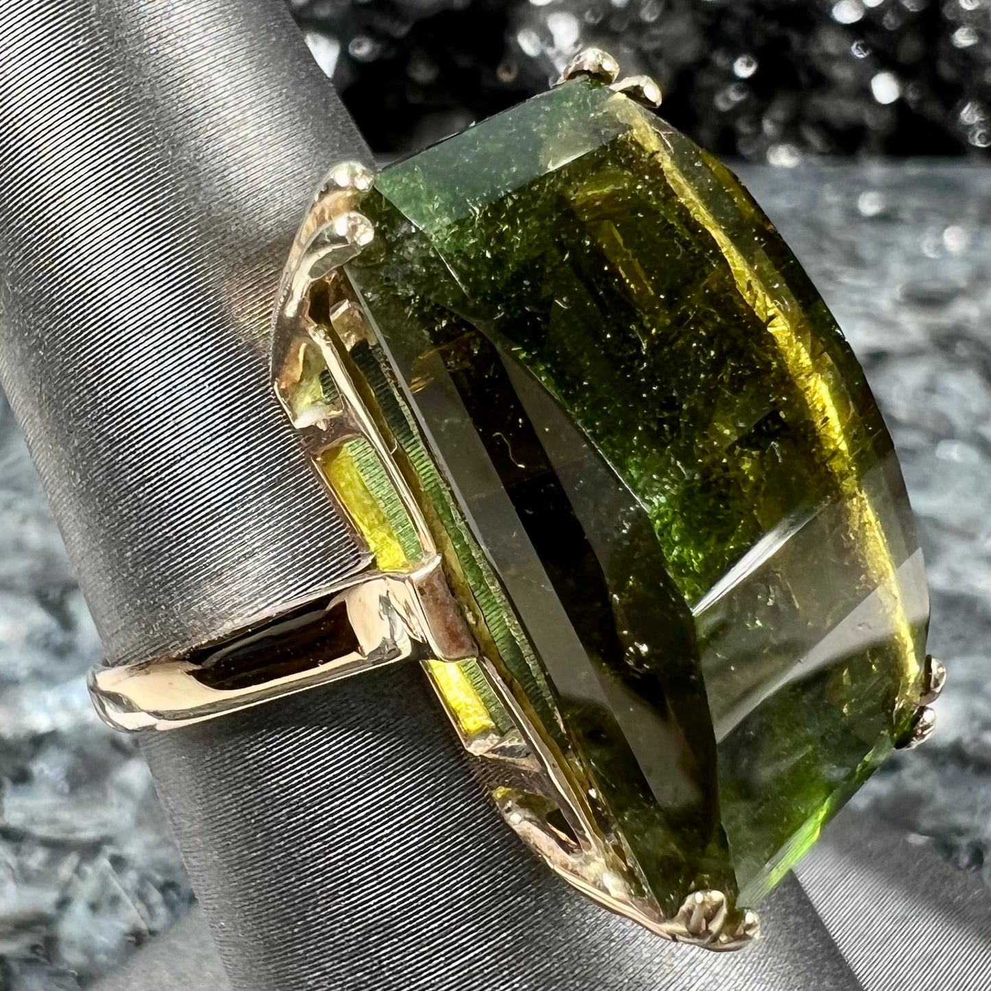 A faceted step-cut dark green tourmaline basket set solitaire ring cast in yellow gold.