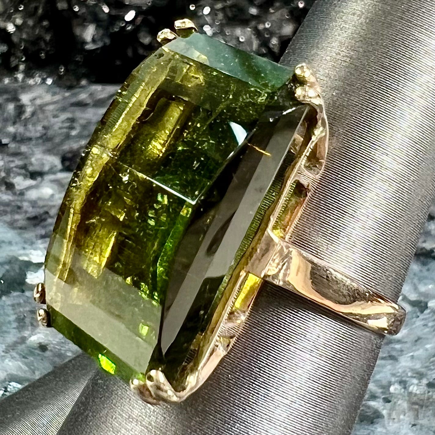 A faceted step-cut dark green tourmaline basket set solitaire ring cast in yellow gold.