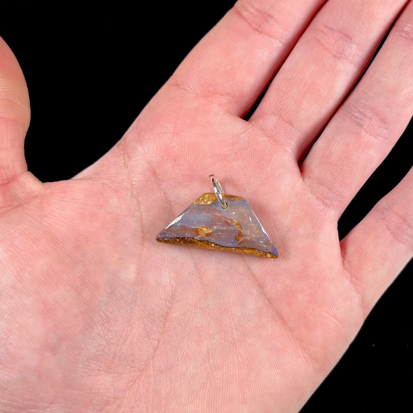 A drilled boulder opal stone with a sterling silver ring through the hole to be worn as a pendant.