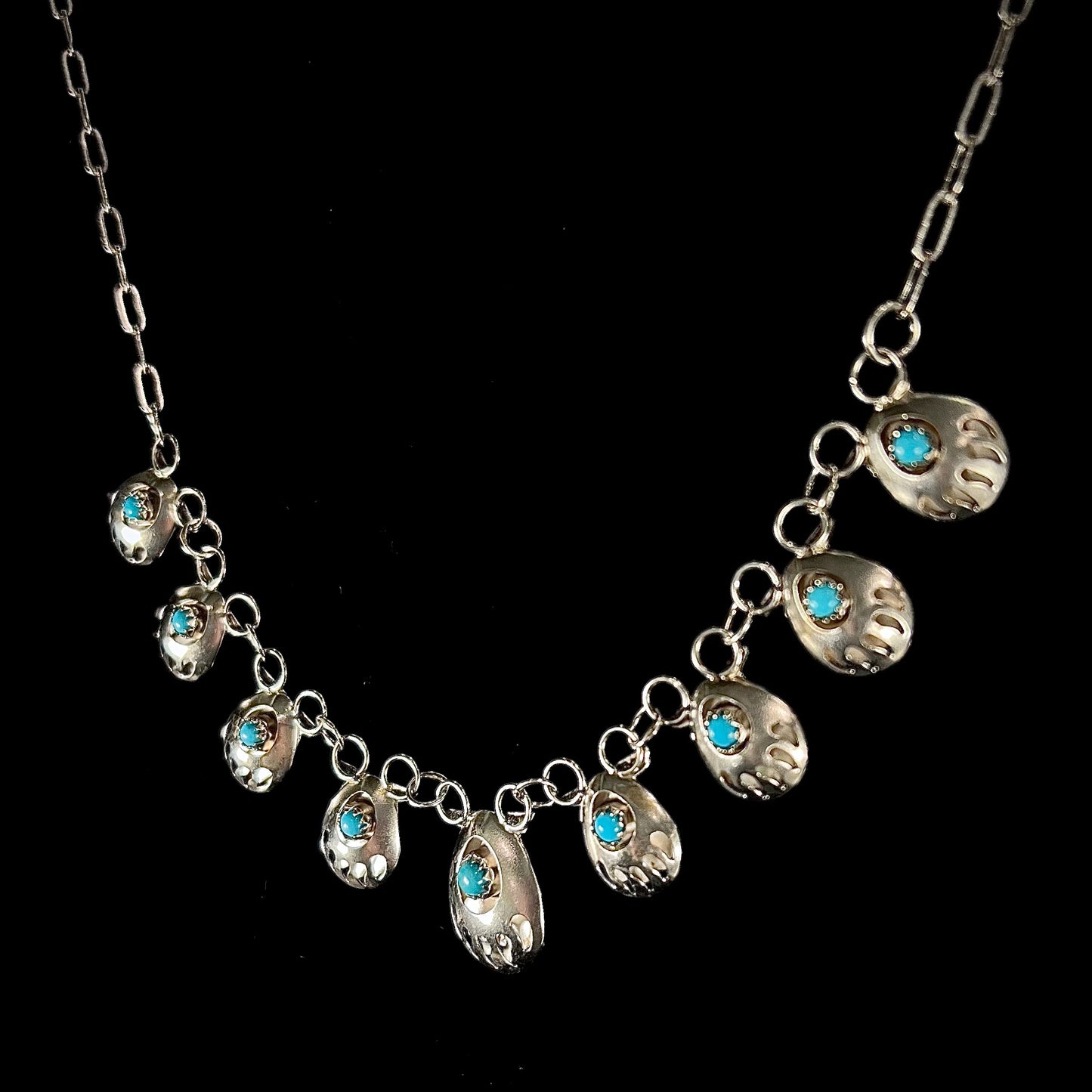 A silver turquoise necklace handmade with nine silver bear paws set with round turquoise stones.