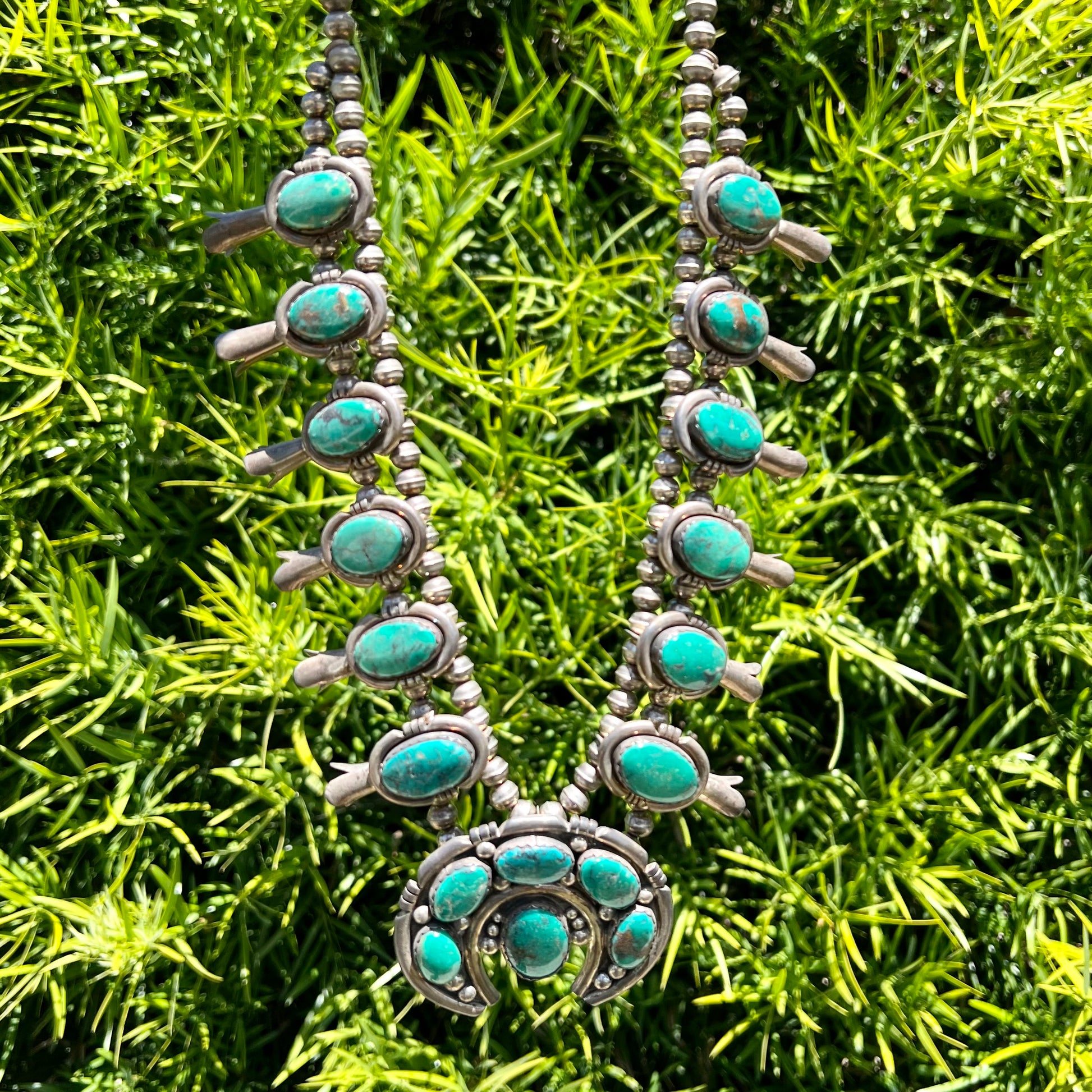 A silver Kingman turquoise squash blossom necklace.  The necklace is made with handmade Navajo pearls.
