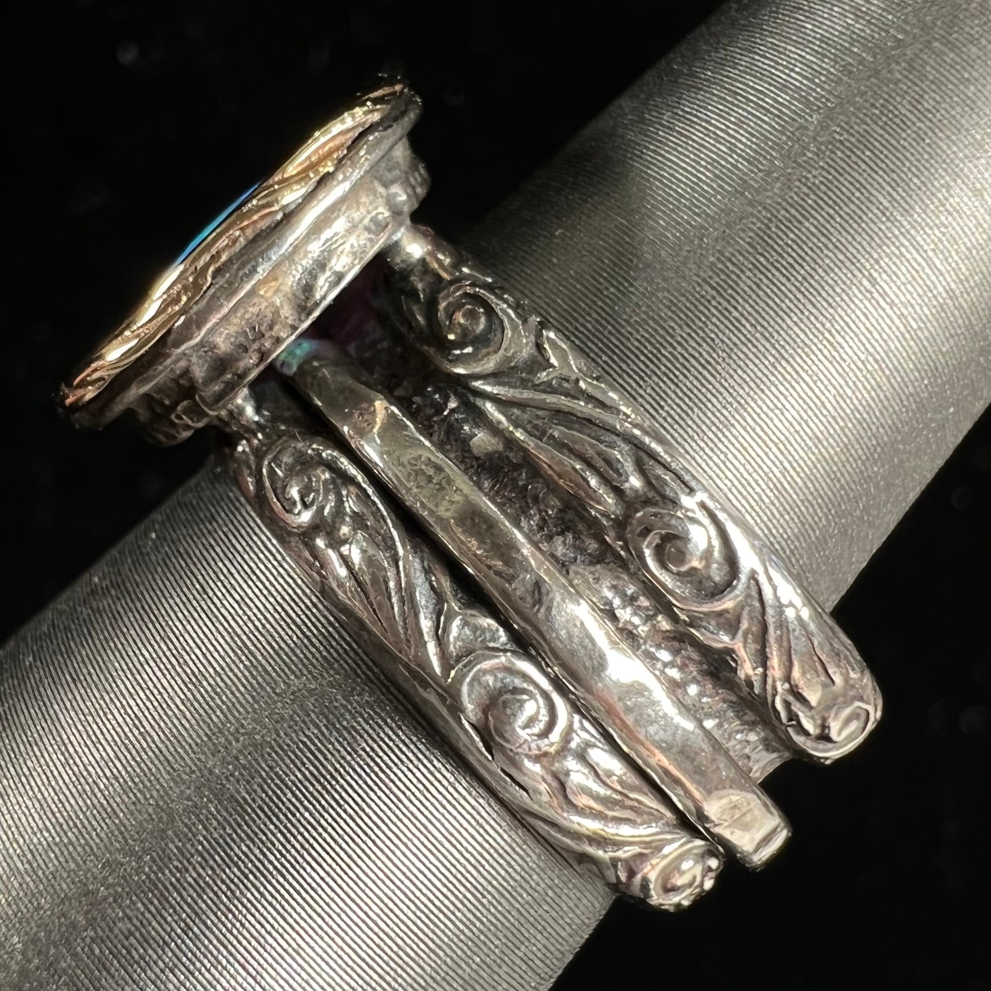 A filigree etched two tone silver and gold spinner ring set with a lab created black opal.