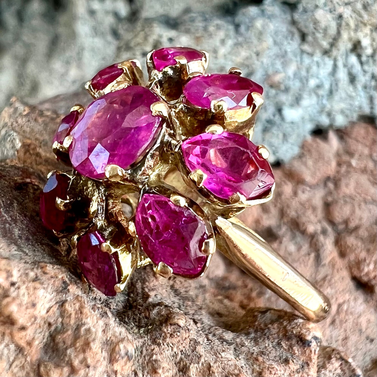 A yellow gold pink Burma ruby cluster ring with a faceted oval center stone surrounded by marquise cut stones.