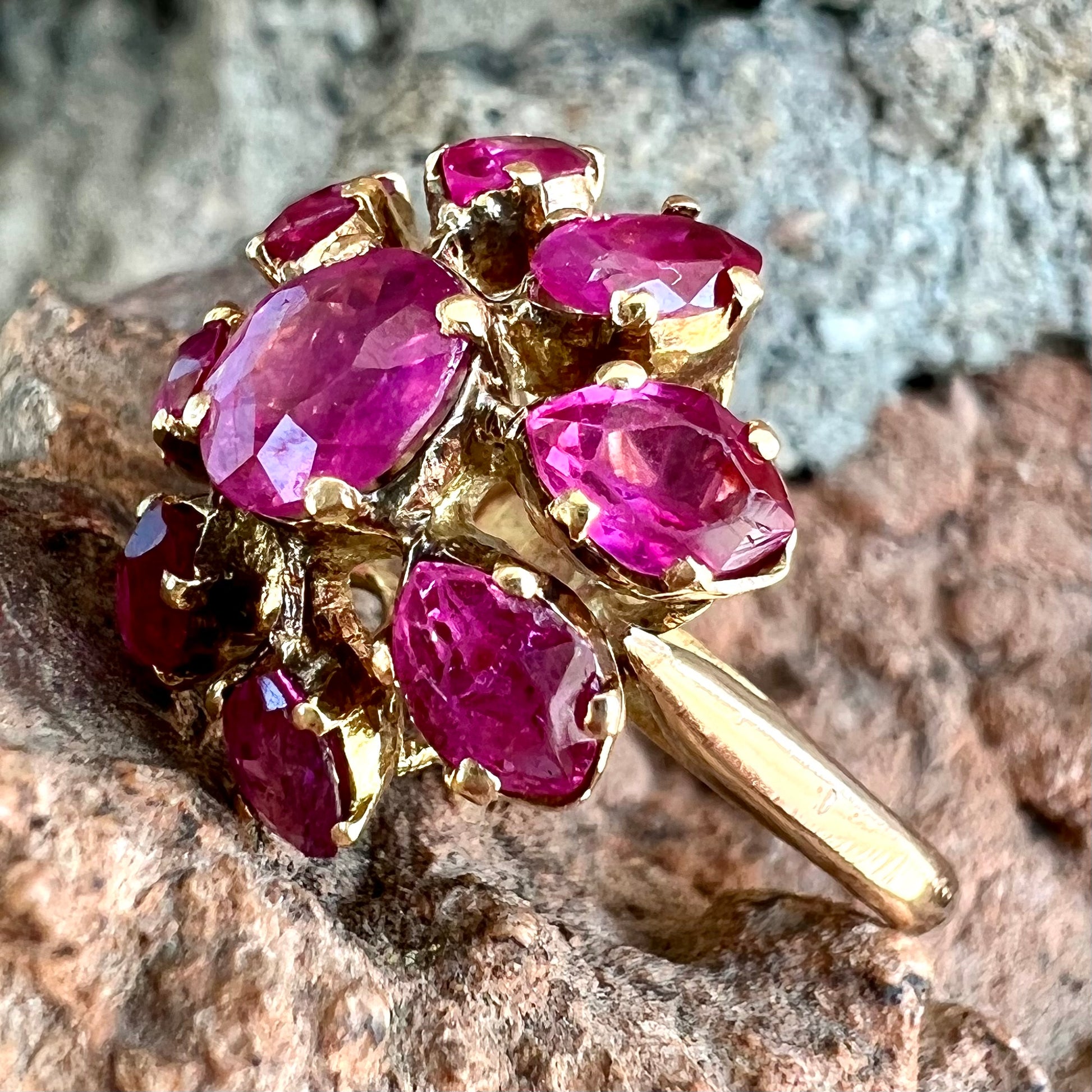 A yellow gold pink Burma ruby cluster ring with a faceted oval center stone surrounded by marquise cut stones.